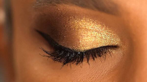 cropped view of african american woman with closed eye and sparkling golden eye shadow