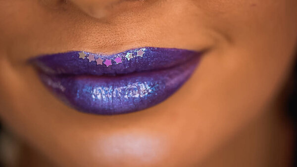 cropped view of smiling woman with stars on purple lips with shimmer