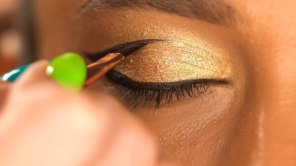 cropped view of african american woman with closed eye applying eye liner