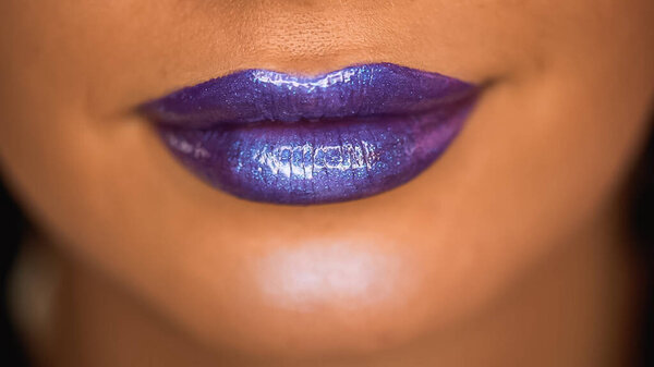 cropped view of woman with shiny lip gloss on purple lips 