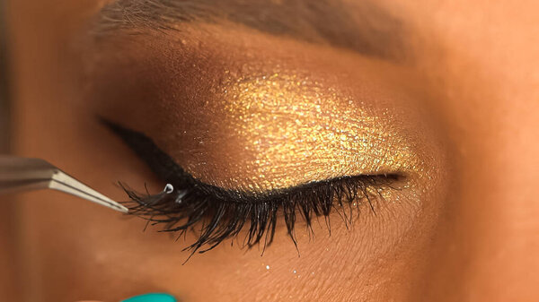 cropped view of african american woman apply false eyelashes with tweezers
