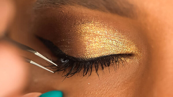 partial view of african american woman apply false eyelashes with tweezers