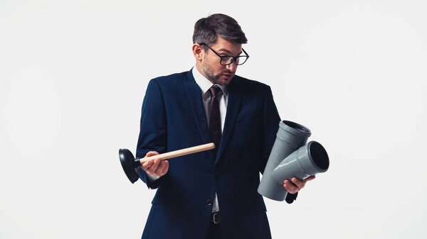 Confused manager in suit holding plastic pipe and plunger isolated on white