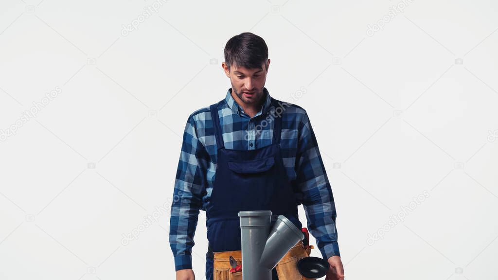 Workman in overalls and tool belt looking at plastic pipe isolated on white