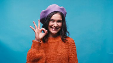 Mor bereli mutlu kadın, mavi renkte izole edilmiş güzel bir jest gösteriyor.