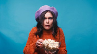 impressed woman with popcorn watching breathtaking movie isolated on blue clipart