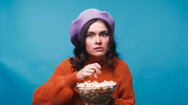 Şok olmuş bir kadın elinde patlamış mısırla tek başına film izliyor.