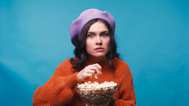 shocked woman holding popcorn while watching movie isolated on blue clipart