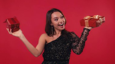 Şaşırmış genç bir kadın elinde kırmızı kutular tutuyor.