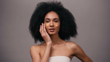 Esmer, Afro-Amerikalı, çıplak omuzlu, göz bantlarını griye yapıştıran bir kadın.