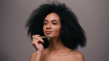 Çıplak omuzlu Afro-Amerikan bir kadın. Gri yolda izole edilmiş yeşil bir silindir kullanıyor.