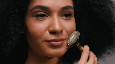 Yeşim silindir kullanan kıvırcık Afrikalı Amerikalı kadının yakın plan fotoğrafı.