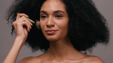 Kıvırcık, genç, Afro-Amerikan kadın. Omuzları çıplak. Yeşim taşı kullanıyor.
