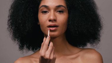 Mutlu Afrikalı Amerikalı kadın gri renge dudak parlatıcısı sürüyor.