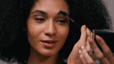Gri kaşlarını fırçalayan Afrikalı Amerikalı genç bir kadına yakından bakın.