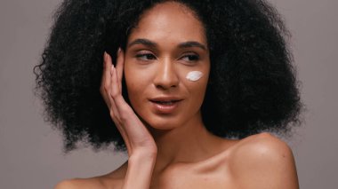 Yüzünde kozmetik kremi olan genç Afrikalı Amerikalı kadın griye izole edilmiş.