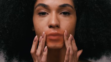 Kolajen dudak bandı süren Afrikalı Amerikalı genç bir kadın. 