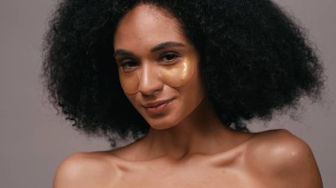 Gri üzerinde izole edilmiş hidrojel göz bantları olan Afrikalı Amerikalı kadına yakın durun.