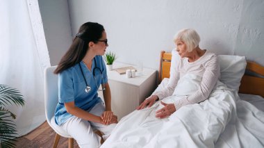 Genç hemşire ve yaşlı kadın klinikte konuşuyor.