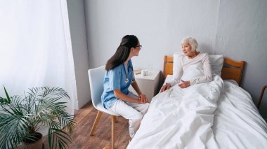 Gözlüklü neşeli hemşire ve klinikte konuşan yaşlı kadın.