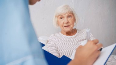 blurred geriatrician writing prescription near aged woman  clipart