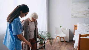 senior woman stepping with walkers near brunette geriatrician nurse clipart