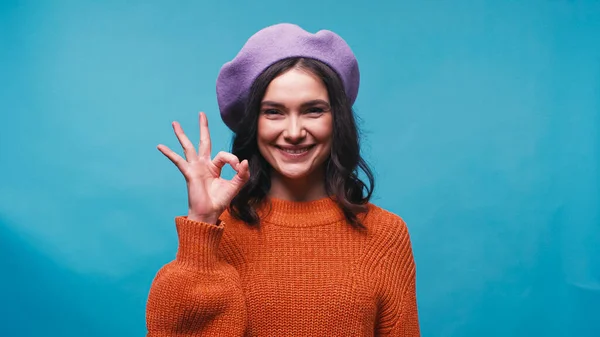 一个身穿淡紫色贝雷帽的积极的年轻女子在蓝色上显得很好的姿势 — 图库照片