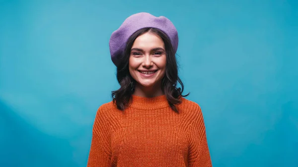 穿着橙色毛衣 头戴紫色贝雷帽的快乐女人 看着被蓝色隔离的相机 — 图库照片