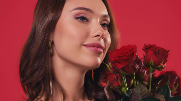 happy young woman smelling roses isolated on red