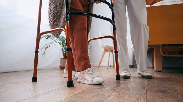 partial view of senior woman stepping with walkers near nurse