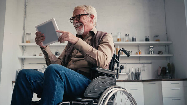 Smiling disabled pensioner in wheelchair using digital tablet at home