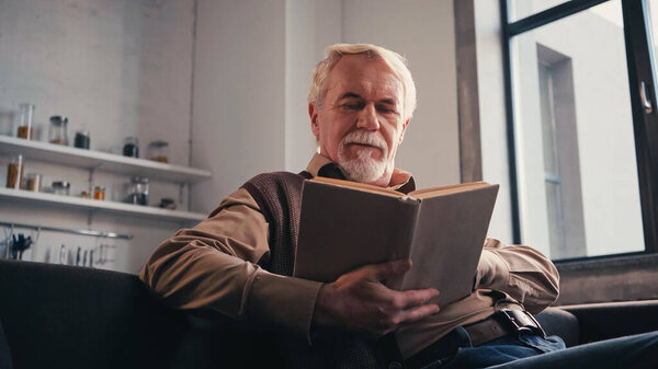 bearded senior man reading book at home 