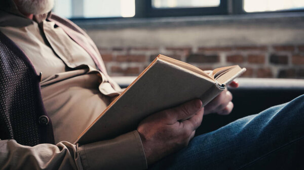 cropped view of bearded senior man reading book at home 