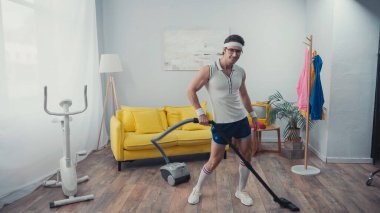 Elektrikli süpürge oturma odasında dans ederken mutlu sporcular, retro spor konsepti