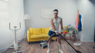 Elektrikli süpürge oturma odasında şarkı söyleyip dans eden sporcu, retro spor konsepti