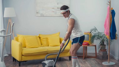 Sporcu elektrikli süpürge oturma odasında şarkı söylerken, retro spor konsepti