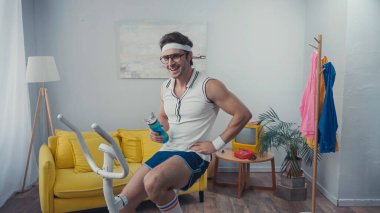 Spor bisikleti antrenmanında ve spor şişesini oturma odasında tutarken mutlu ol, retro spor kavramı.