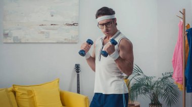 Oturma odasında dambılları kaldıran güçlü bir adam, retro spor konsepti