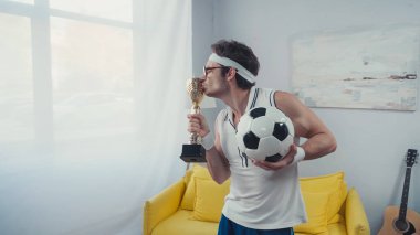 Futbolcu altın kupayı öpüyor ve futbol topu tutuyor.