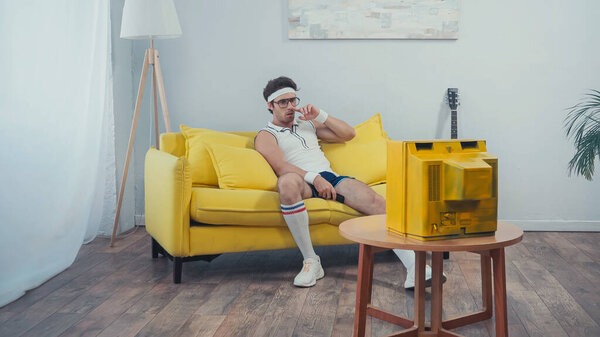 lazy man in sportswear picking nose while sitting on sofa in living room