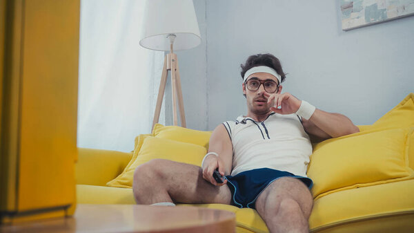 lazy man in sportswear picking nose while sitting on sofa and clicking channels 