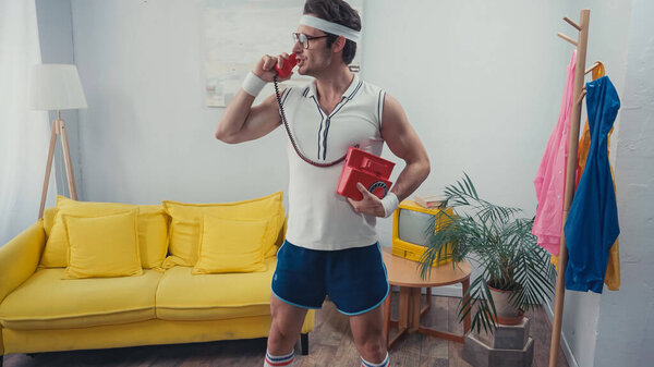 Sportsman in eyeglasses standing while talking on landline telephone in living room