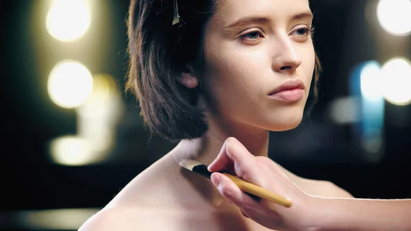 Maquillador aplicando fundación sobre clavículas de modelo morena con pincel cosmético - foto de stock