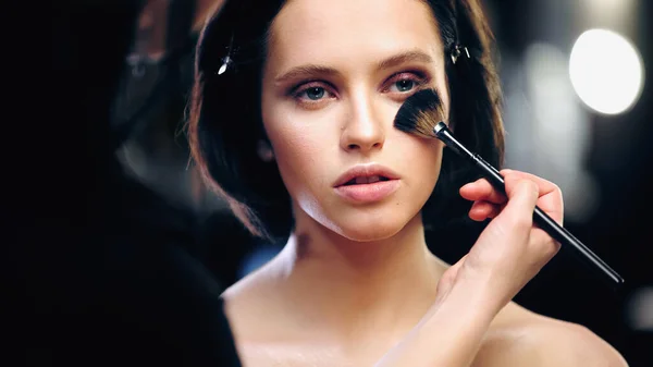 Maquillador aplicando polvo facial en la cara del modelo con hombros desnudos - foto de stock