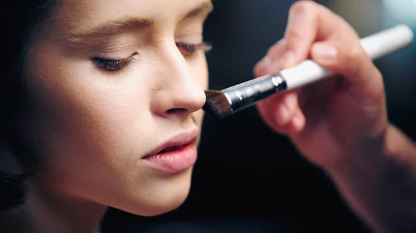 Close up de maquiador aplicando base de maquiagem na pele do modelo com escova cosmética — Fotografia de Stock