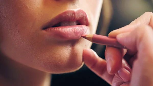 Vue recadrée du maquilleur appliquant crayon à lèvres sur les lèvres de la jeune femme — Photo de stock