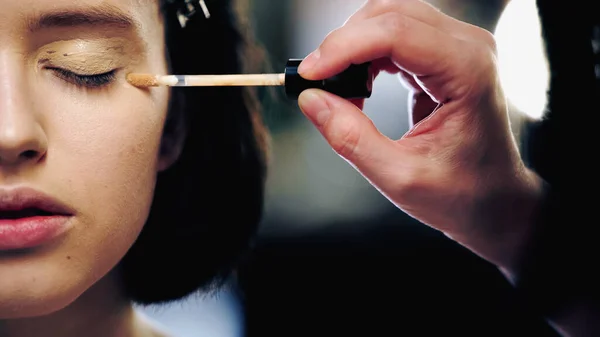 Visão recortada do artista de maquiagem aplicando corretor na pálpebra da mulher — Fotografia de Stock