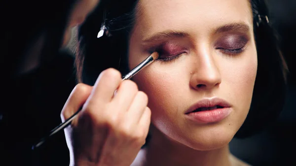 Trucco artista applicando ombretto con pennello cosmetico sul modello — Foto stock