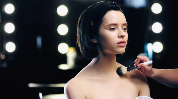 Makeup artist applying powder on clavicles of pretty model with bare shoulders — Stock Photo