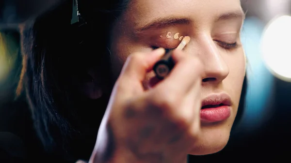Makeup artist applying concealer on eyelid of woman — Stock Photo